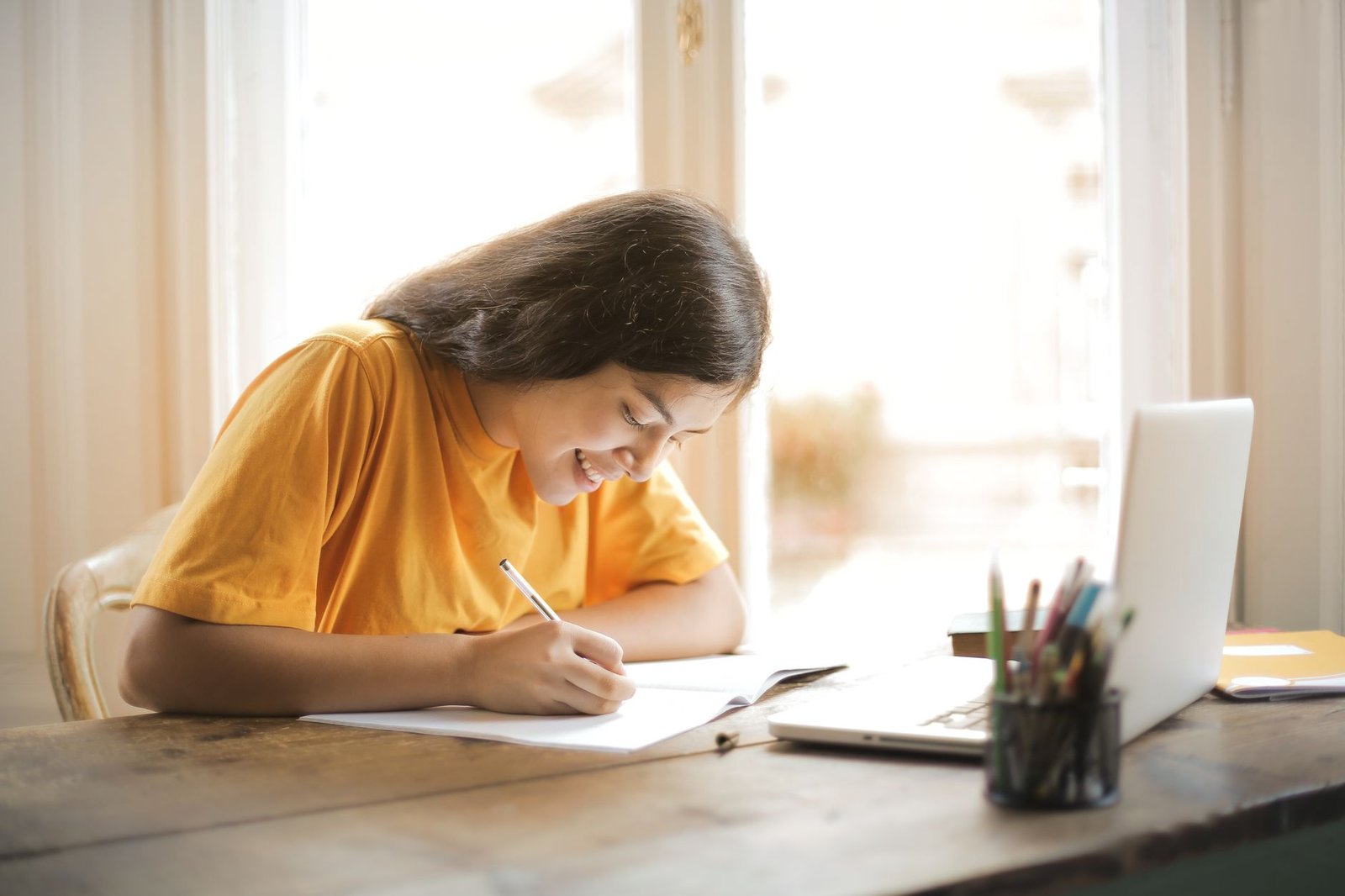 Student writing by hand at a sunlit desk